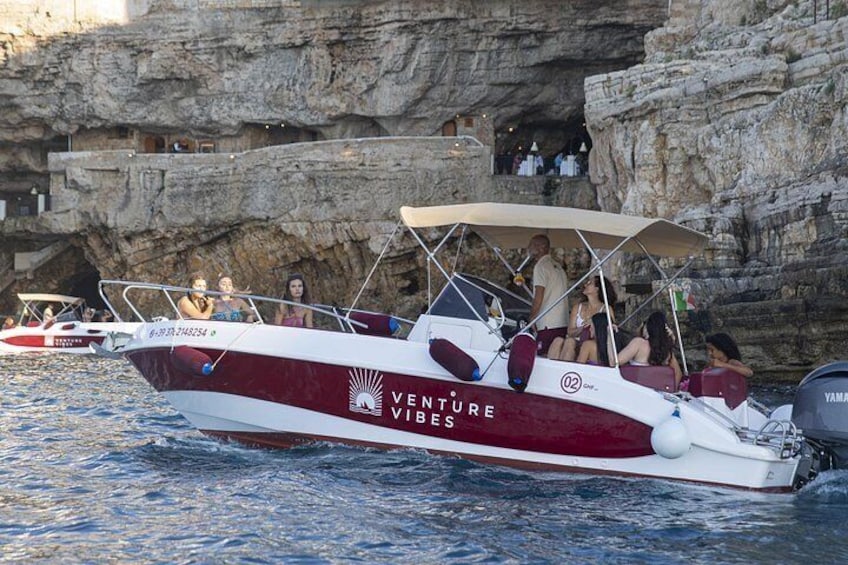 Un barco llamado 'Venture Vibes' con pasajeros, anclado cerca de acantilados rocosos. 2