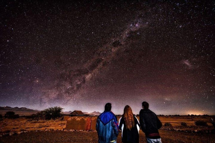 A starry night sky with the Milky Way visible, a desert landscape, and three people standing in the foreground. 4
