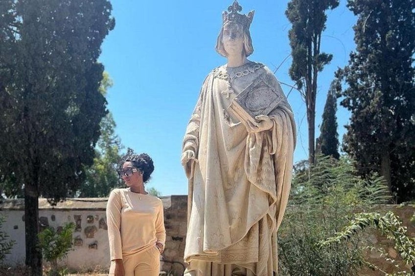 A statue of a historical figure in a robe, standing in a garden with trees and a clear sky. 2