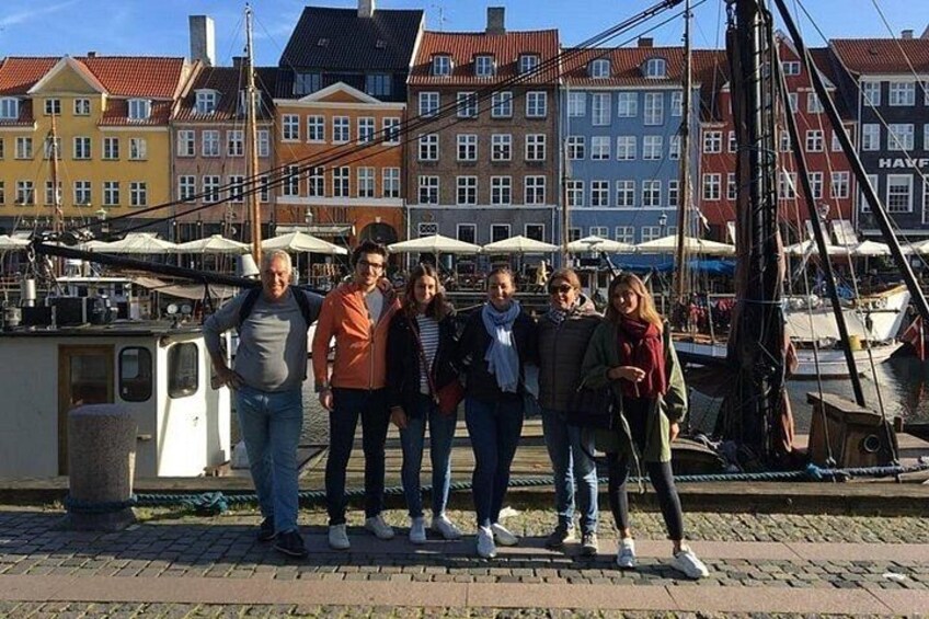 En gruppe mennesker står på en bro ved siden af en lysthavn med farverige bygninger i baggrunden. 5