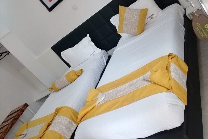 A bed with white and yellow bedding, a dark headboard, and a wall-mounted clock. 4