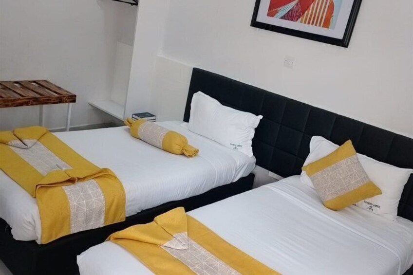 Two beds with white and yellow bedding, a wooden table, and a framed picture on the wall. 5