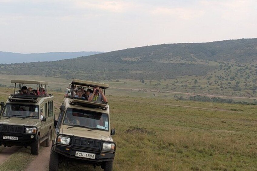Two safari vehicles on a dirt road with a hilly landscape in the background. 2
