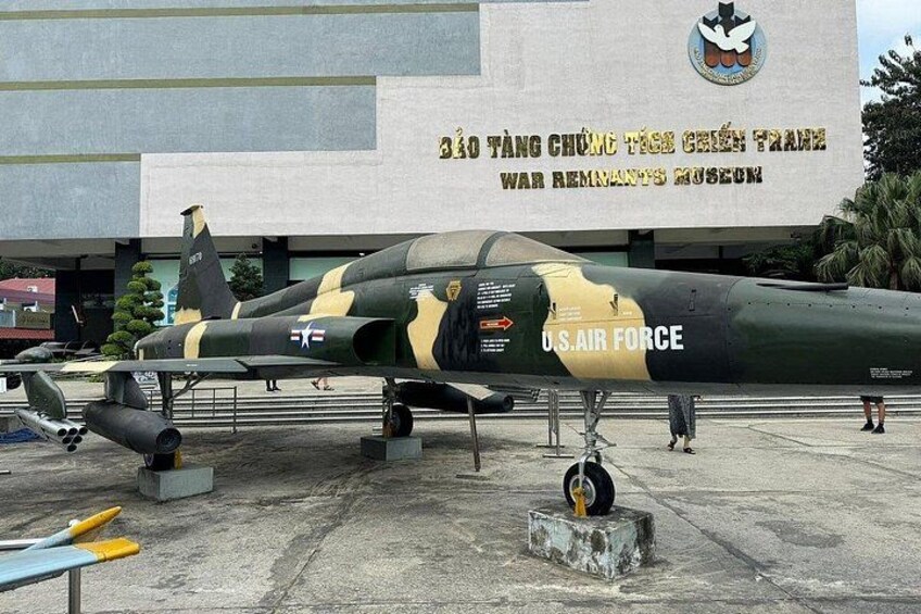 Un avión militar con los marcados 'Fuerza Aérea de los Estados Unidos' y 'TF', estacionado frente a un edificio con un letrero que dice 'Museo de las Secuelas de la Guerra'. 5