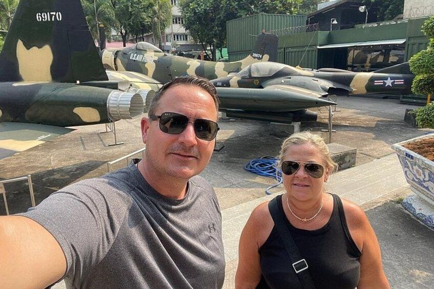 Un hombre y una mujer tomando un selfie con aviones militares al fondo. 2