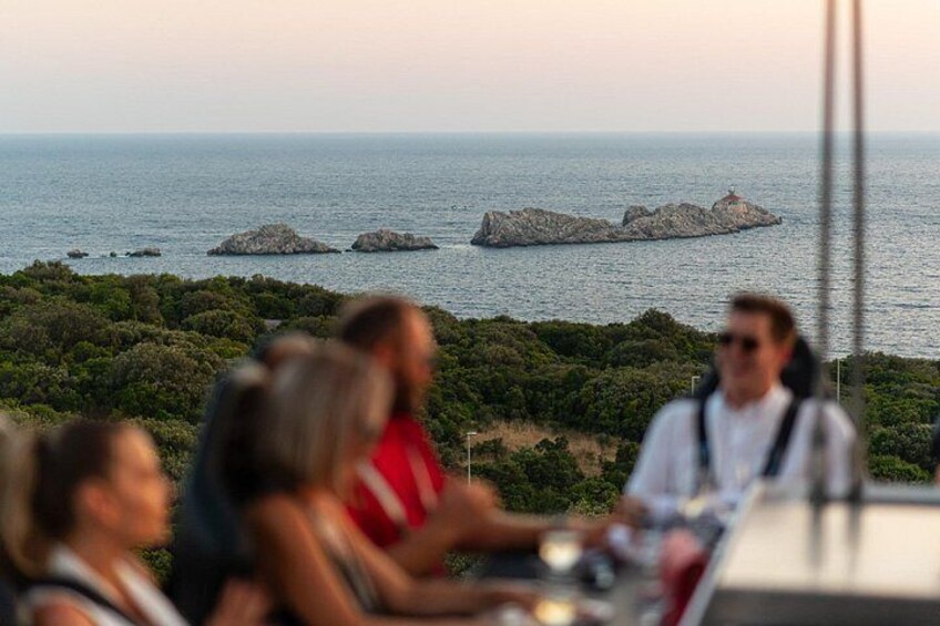 A group of people dining at a table with a scenic view of the ocean and rocky islands. 4