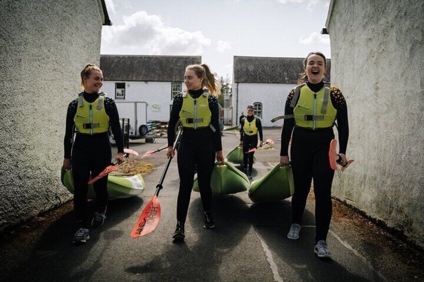 Three people in wetsuits carrying kayaks and paddles, walking on a road. 2