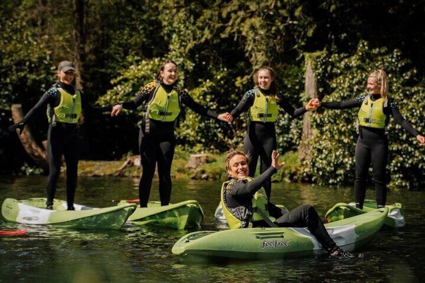 People on a green inflatable raft, wearing life jackets, in a forested area. 4