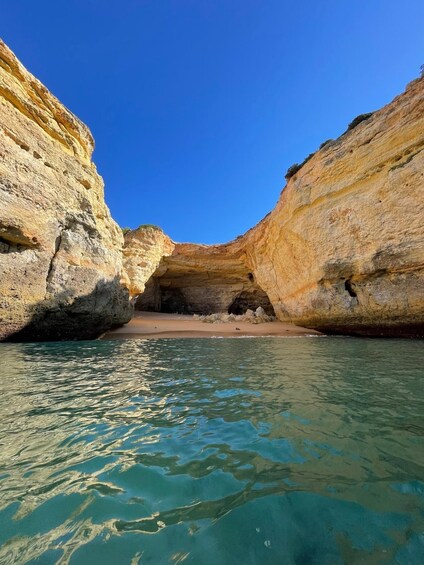 A coastal cave entrance with clear turquoise water and sandy beach. 3