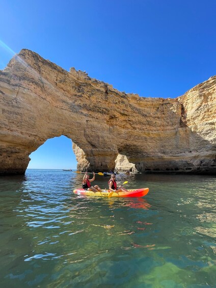 Two people kayaking under a large rock arch. 2