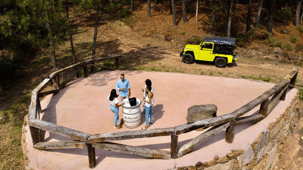 A group of people around a barrel labeled 'Valminor' in a fenced outdoor area with a yellow vehicle in the background. 3