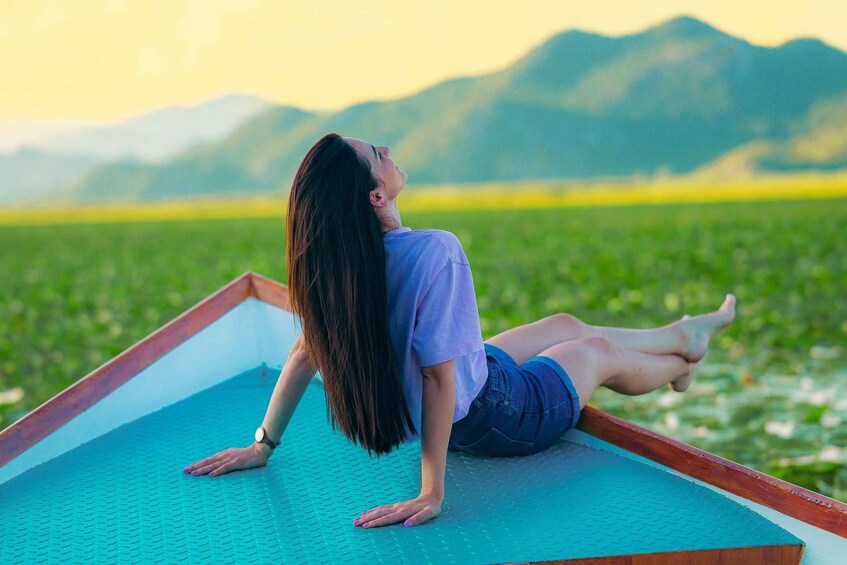 A person lying on a blue mat outdoors with a mountainous landscape in the background. 1