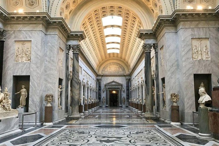 A grand hallway with marble floors, classical columns, and statues. 2