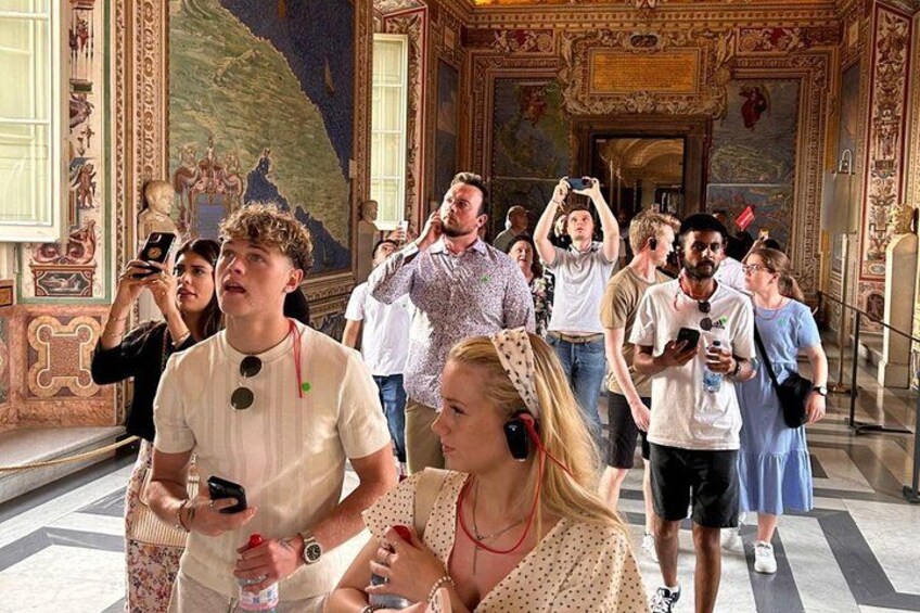 A group of people in a grand, ornately decorated room with a large mural on the wall. 1