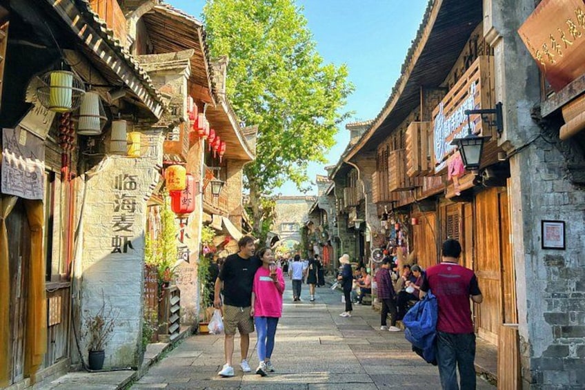 A narrow street lined with traditional buildings, some with signs in a foreign script, and people walking. 2