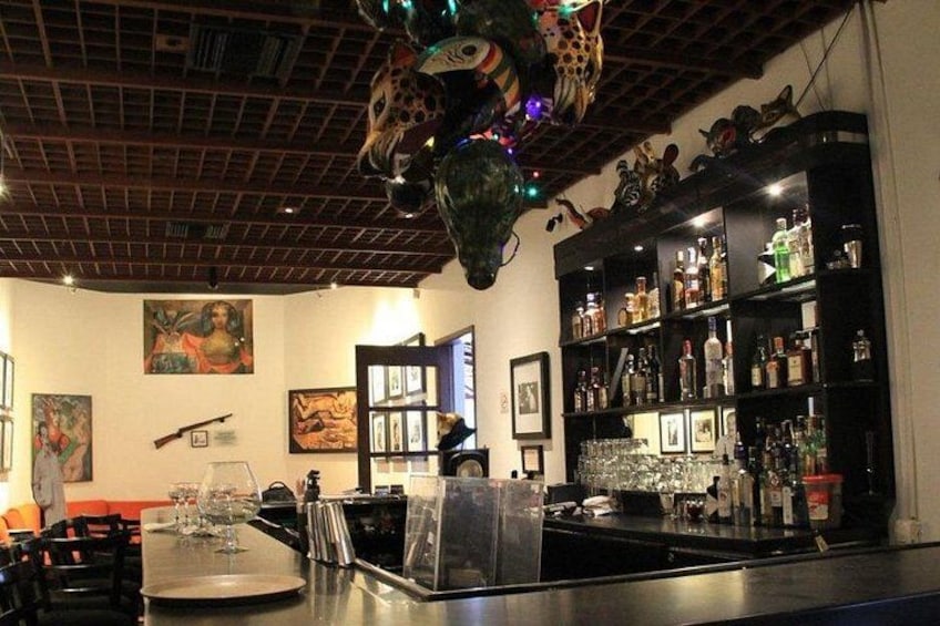 A bar with a counter, shelves of bottles, and framed pictures on the wall. 3