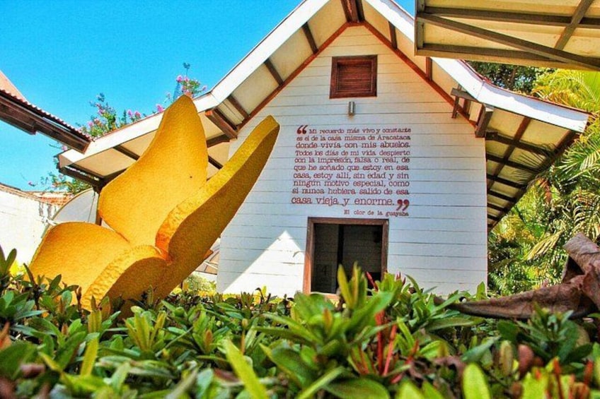 A white building with a roof, surrounded by greenery and a large yellow sculpture. 2