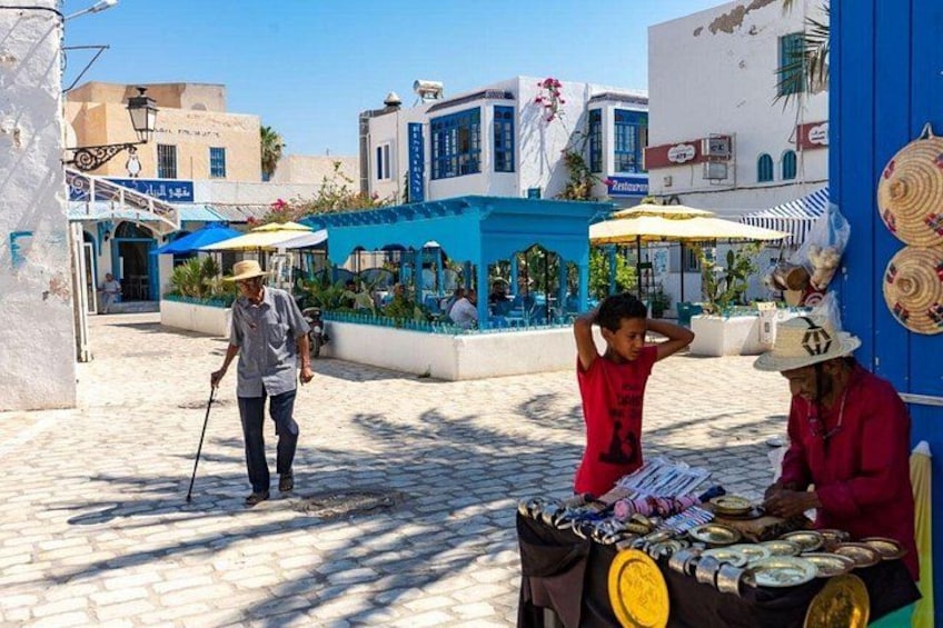Una calle adoquinada con un hombre caminando y dos mujeres vendiendo sombreros. 5