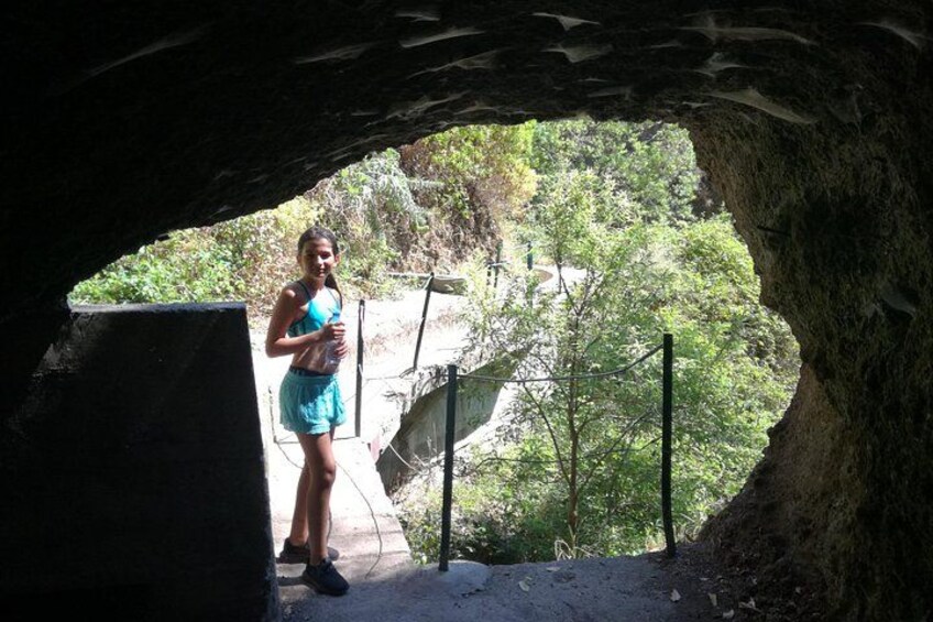 A person standing in a cave entrance with a view of a forested area and a staircase. 2