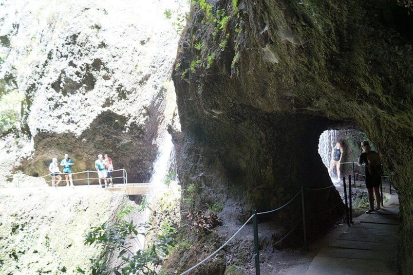 A cave entrance with a viewing platform, a waterfall, and a person taking a photo. 3