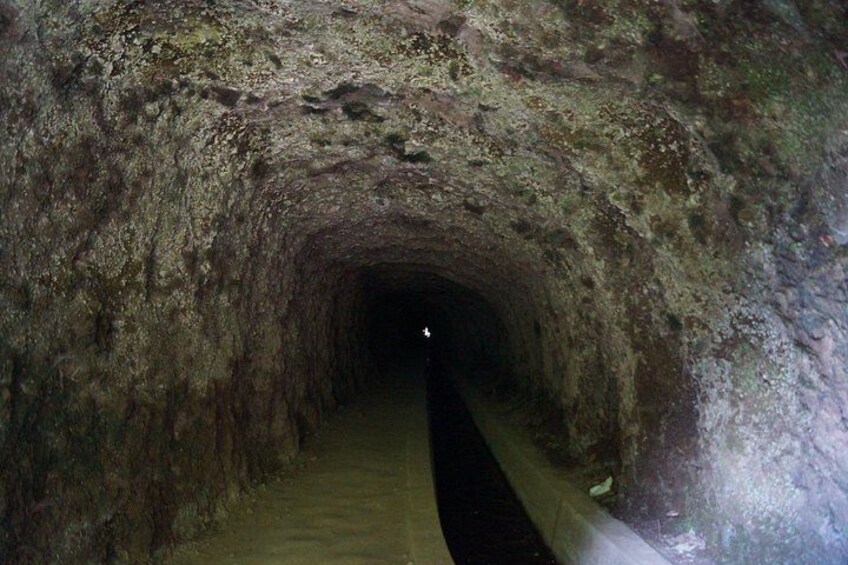 A narrow, dimly lit tunnel with rough, uneven walls and a concrete path. 4