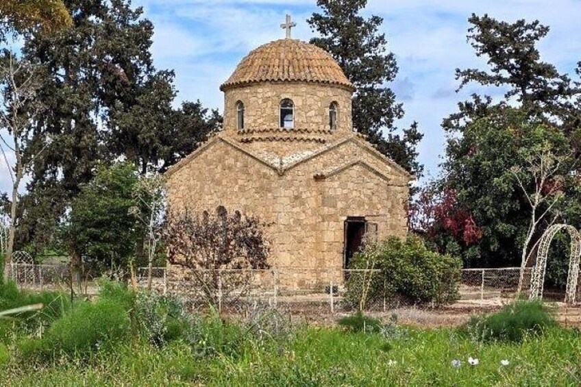A small stone church with a dome and bell tower, surrounded by trees and grass. 1