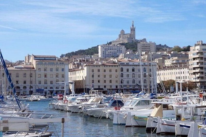 A marina with boats docked, buildings, and a hill with a tower in the background. 2