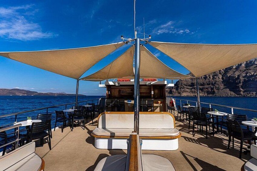 A boat deck with outdoor seating, a bar, and a view of the sea and rocky coastline. 2