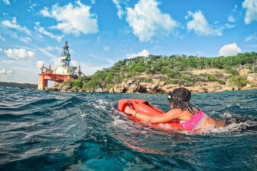 A person on a red raft in the ocean, with a lighthouse and rocky shoreline in the background. 2