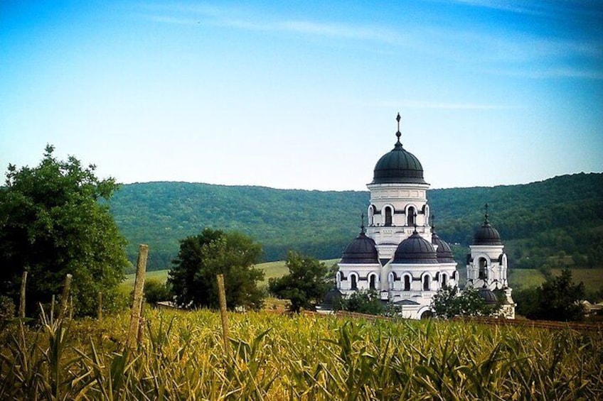 A white church with multiple domes surrounded by a field and hills in the background. 1