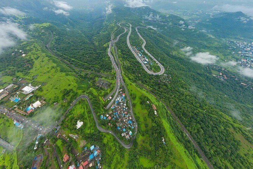 A winding road through a mountainous area with scattered buildings and greenery. 1
