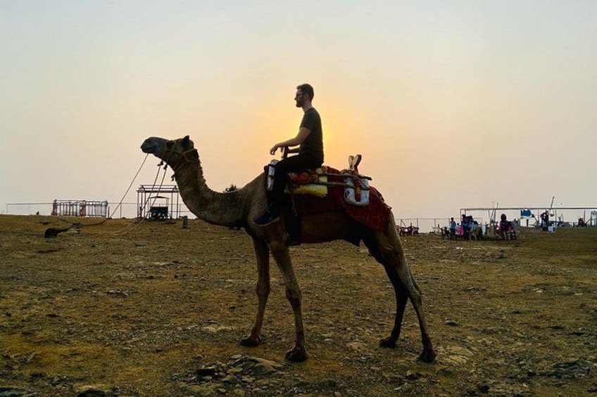 A camel with a rider in a desert setting during sunset. 3