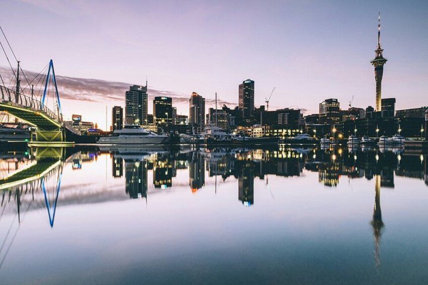 Un horizonte urbano con una torre destacada, un puente y un muelle tranquilo que refleja los edificios. 3