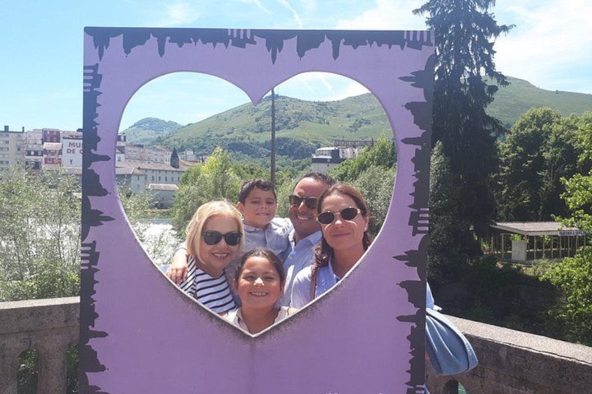 Un grupo de personas posando frente a una estructura con forma de corazón, con vistas panorámicas de colinas y edificios al fondo. 2