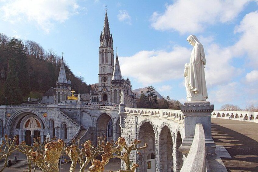 A historic church with a tall spire, a statue, and a stone bridge. 1