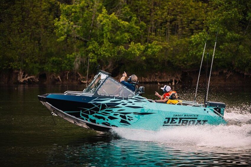 A speedboat with 'JETBOAT' and 'SMOKY MOUNTAIN' written on it, moving through water with a forested background. 5