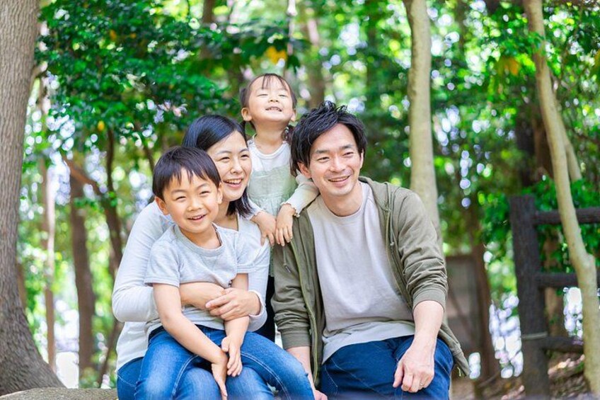 Una famiglia di quattro persone seduta su una panchina in una zona boschiva, con alberi e un recinto di legno sullo sfondo. 5