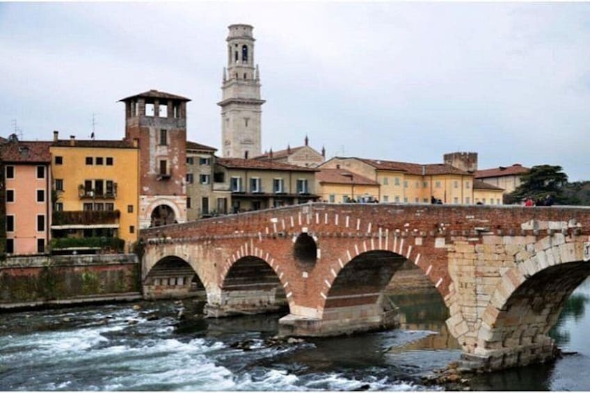 A stone bridge over a river with buildings and a tower in the background. 4