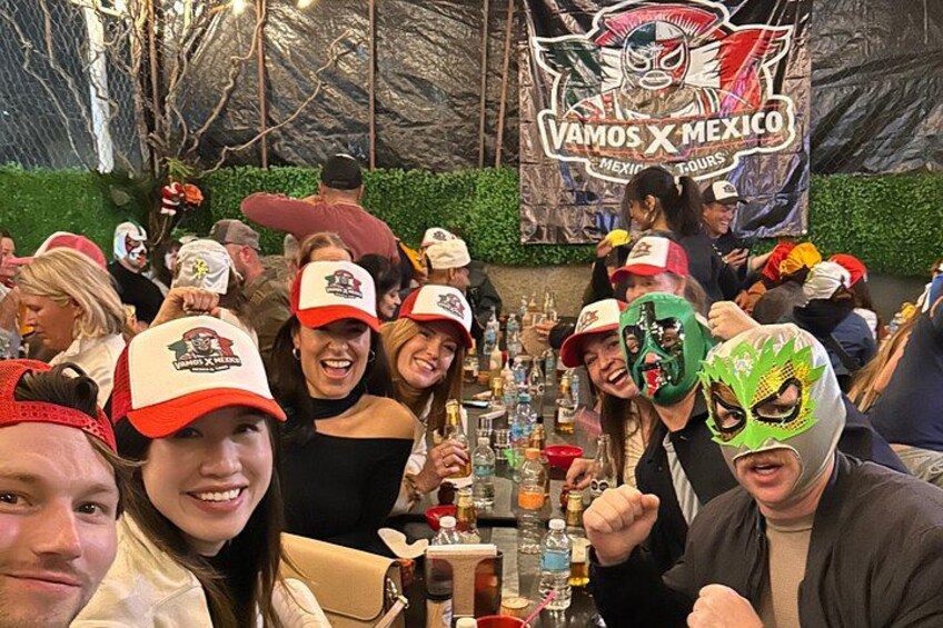 Un grupo de personas en un evento con un cartel que dice 'Vamos X Mexico' y una barra con varias botellas. 3