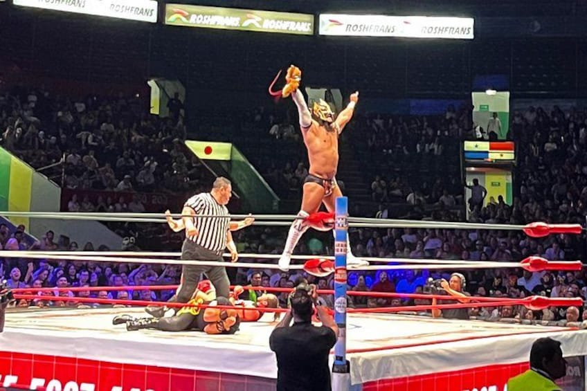 A wrestling ring with a referee and a wrestler in a victory pose. 2