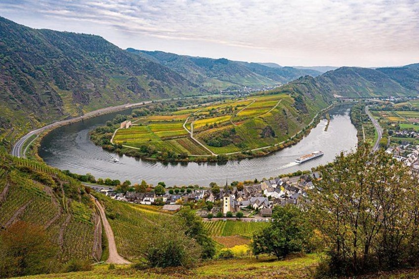 A river curving through a valley with vineyards, a town, and hills in the background. 5