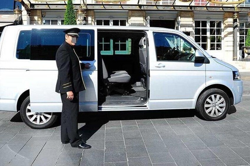 A white van with its door open, a man in uniform standing beside it, and a building with classical architecture in the background. 4