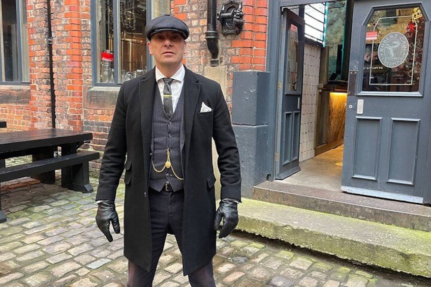 Una persona con un traje antiguo frente a un edificio de ladrillo con puerta y ventanas. 4