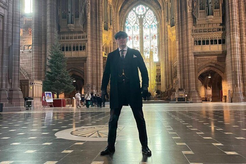 Una persona vestida con traje está de pie en una catedral con un gran ventanal de vitrales y un diseño de suelo circular. 3