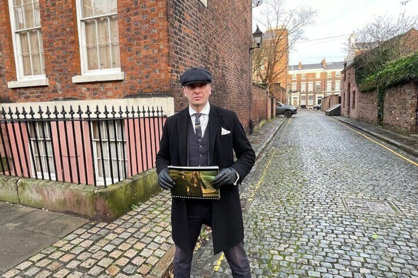 A person in a suit holding a book on a cobblestone street. 4