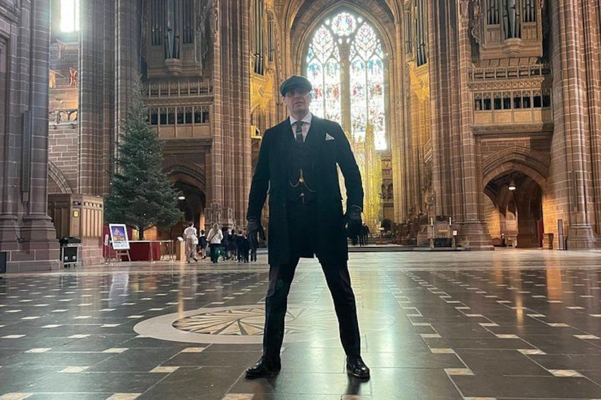 A person standing in a cathedral with a large stained glass window in the background. 2