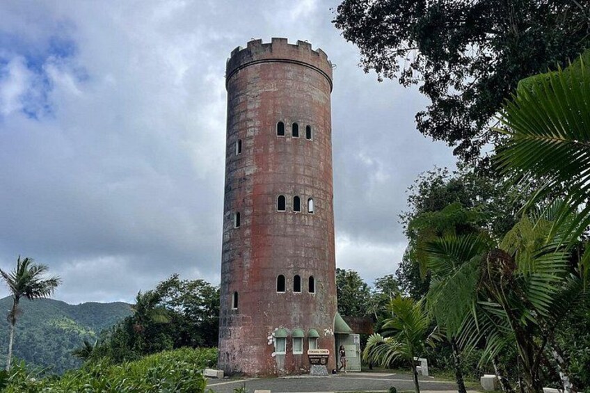 A tall, cylindrical brick tower with multiple windows, surrounded by lush greenery and hills in the background. 4