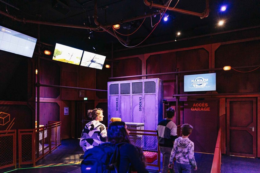 An indoor space with multiple screens, a large purple storage unit labeled 'STOCK-V1' and 'STOCK-V2', and a sign reading 'NAMAZU'. 2