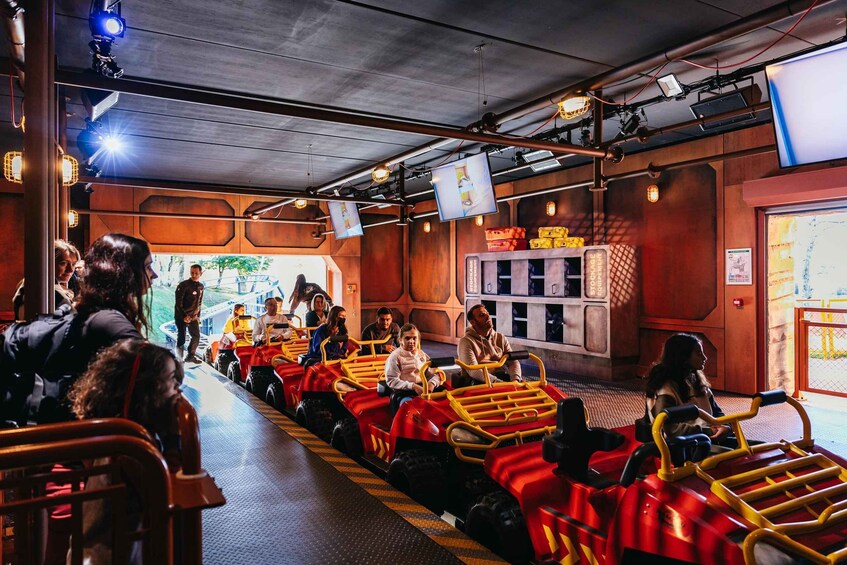 A ride with red and yellow vehicles, people waiting, and a ticket booth. 3