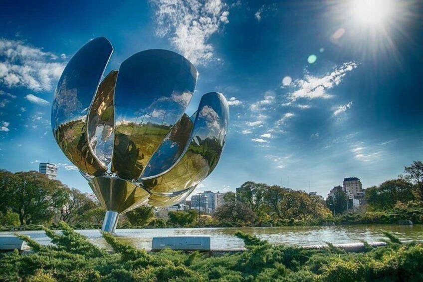 Una scultura metallica in un parco, con uno specchio d'acqua e edifici cittadini sullo sfondo. 2